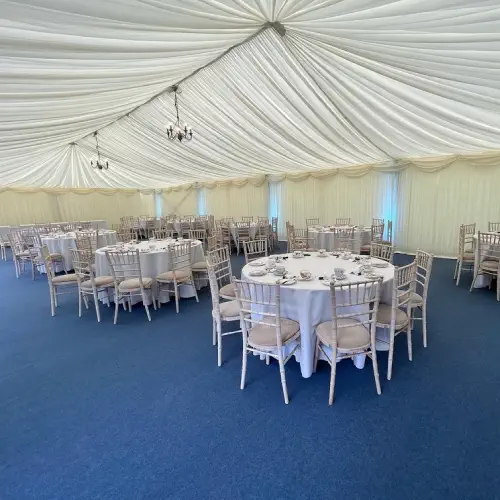 Elegant Melody Corporation marquee interior with round tables set for dining, white draped ceilings, and chandeliers.